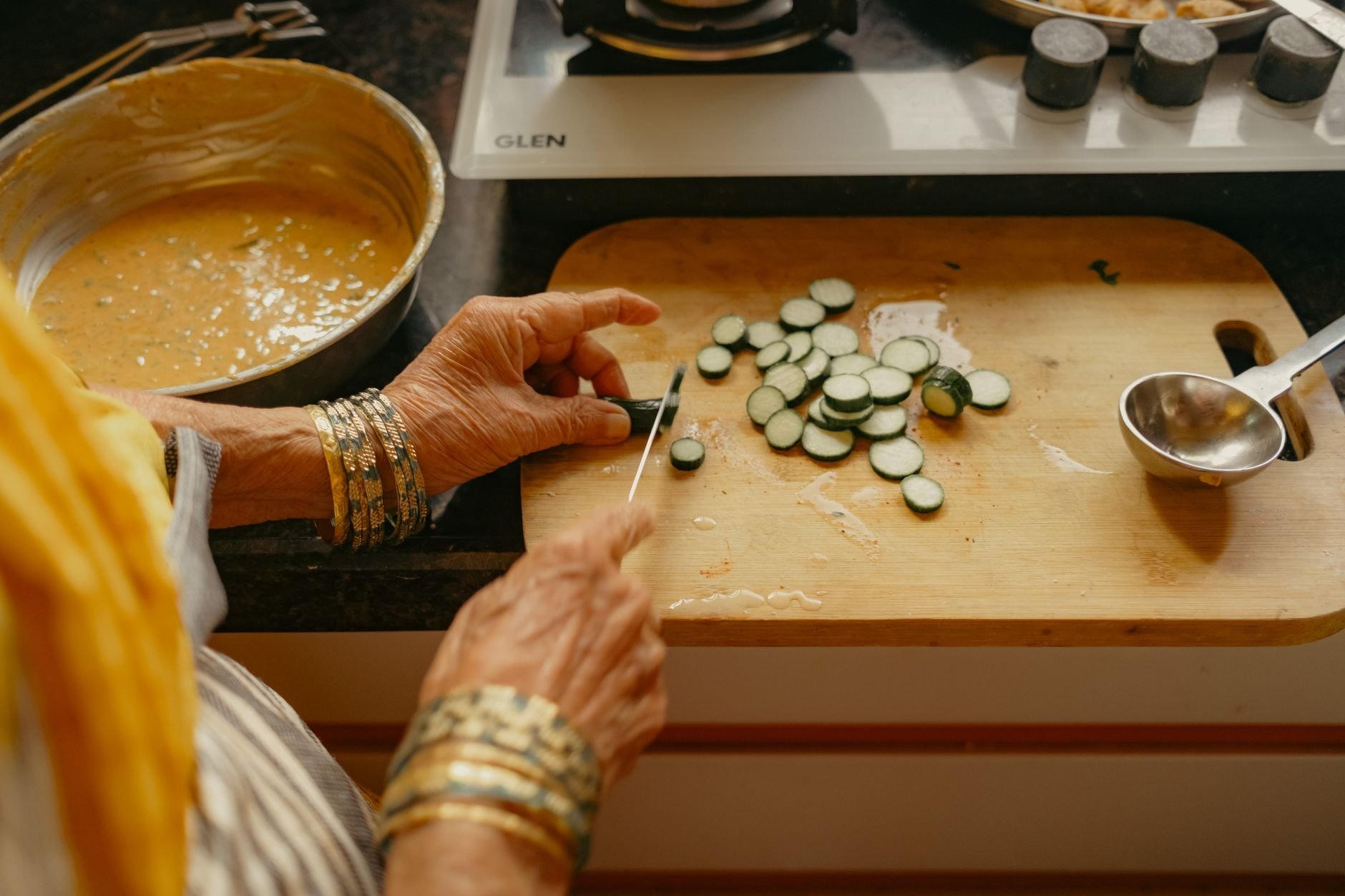 Senior Indian woman chops vegetables in a kitchen, preparing a meal with traditional methods.